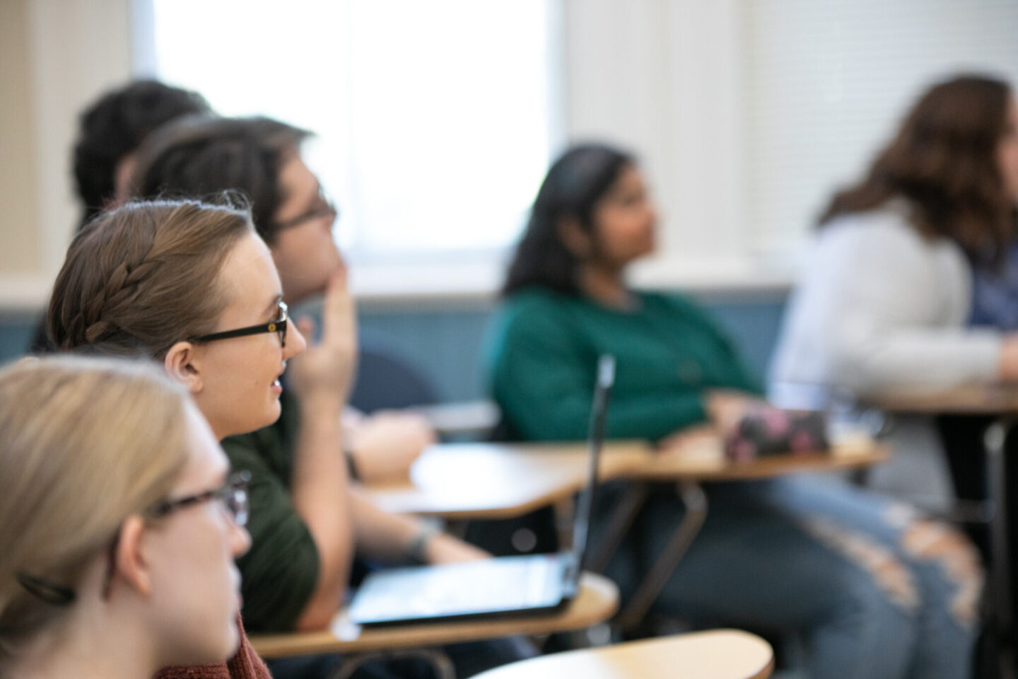 Side view of students sitting in desks listening and engaged in a college lesson