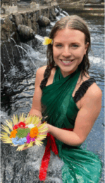 a female counseling student standing in a river while holding a leaf covered in colored powder