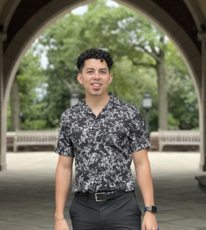 Dr. Cristian Padilla Romero is posing, wearing a paisley printed black and grey short sleeve button up